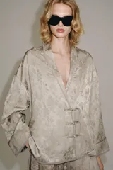 Blazer de estilo oriental confeccionado en hilatura de viscosa con tejido jacquard tono sobre tono. Presenta escote en pico, manga larga y cierre frontal cruzado con alamares a tono.