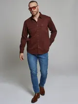 Camisa de manga larga color marrón, con cuello clásico, cierre frontal con botones y dos bolsillos frontales con solapa en el pecho.