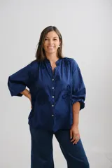 Blusa azul marino de corte holgado, con cuello mao y cierre frontal de botones. Presenta mangas tres cuartos con puños elásticos y un delicado diseño de bordados florales en relieve distribuidos por toda la prenda.