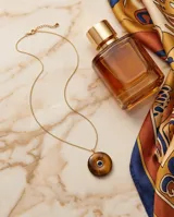 Collar de cadena fina con baño de oro y dije circular de piedra natural ojo de tigre con una circonia azul engastada en el centro.