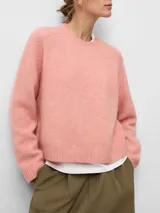 Jersey de punto corto en color rosa, con cuello redondo, manga larga y terminaciones en canalé. Confeccionado en una mezcla de lana merino, alpaca y poliamida, ofreciendo una textura suave y cálida.