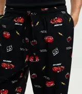Pantalón de pijama de plush color negro con estampado de autos rojos, corte holgado, cintura elástica con cordón de ajuste y puños en los tobillos.