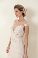Vestido largo de novia color marfil, de encaje y tul, con apliques bordados y piedras. Tiene escote profundo y falda con cola.