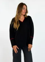 Sweater de punto negro con cuello en V y detalles en color bordó en el borde del cuello y en los puños. Presenta un diseño holgado de manga larga con puños acanalados.