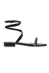 Sandalia flat negra con textura de piel de serpiente, tira delantera con strass y pulsera al tobillo con hebilla.