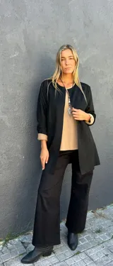 Chaqueta negra de corte recto y largo medio, con cuello redondo sin solapas y mangas largas con vuelta en color beige en los puños.