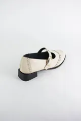 Zapato tipo guillermina estilo oxford, confeccionado en cuero negro con detalles de perforaciones decorativas en la puntera y cierre mediante tira con hebilla metálica dorada. Presenta un taco bajo cuadrado.