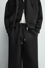 Pantalón de corte wide fit confeccionado en tejido técnico con efecto neopreno. Presenta cintura elástica ajustable con cordón, perneras anchas con costura frontal, bolsillos laterales y bolsillos traseros de plastrón.
