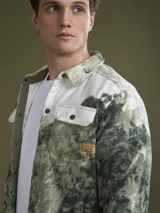 Camisa tipo chaqueta de polar con estampado de camuflaje en tonos verde y blanco, con cuello clásico, cierre frontal con botones a presión, dos bolsillos de parche en el pecho y puños abotonados.