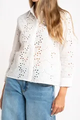 Blusa blanca de manga larga con cuello camisero y bordado tipo broderie anglaise con diseño floral calado.