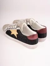 Championes de cuero sintético color beige con detalles en plateado y negro. Presentan una estrella dorada en el lateral y cordones blancos.