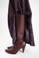 Bota de caña alta confeccionada en cuero vegano color negro, con punta fina y taco cónico de altura media.