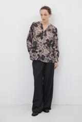 Camisa de corte recto con estampado floral en tonos beige y negro, cuello mao con escote en V y cierre frontal parcial con botones. Presenta mangas tres cuartos con detalle de trabilla para ajustar.