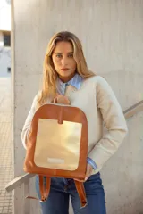 Mochila de cuero color tostado con bolsillo frontal dorado y cierre plateado.