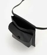 Billetera crossbody de poliuretano color negro, de diseño compacto y moderno con compartimento principal y bolsillo frontal con solapa y cierre a presión. Cuenta con asa larga para uso cruzado.