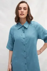Vestido camisero midi de lino color celeste, con abotonadura frontal completa, manga corta ranglan, bolsillos laterales y volante en el ruedo.