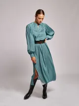 Vestido midi de satén con estampado geométrico en tonos marrones y naranjas. Presenta cuello mao, mangas largas abullonadas con puños ajustados y un cinturón a tono con hebilla metálica que marca la cintura.