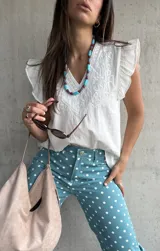 Musculosa blanca de diseño ligero con escote en V y sutiles detalles bordados tonales en el frente, complementada con volados en las sisas.
