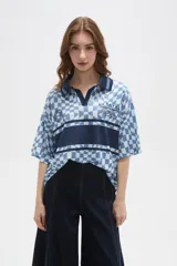 Remera tipo chomba de manga corta con cuello camisero, confeccionada en tejido con estampado de tablero ondulado en tonos rosado y blanco, con franja horizontal y detalles gráficos en color bordó.