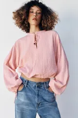 Blusa de manga larga con estampado de cuadros vichy en tonos rosado y blanco. Presenta cuello redondo con volante, cordón ajustable en el escote con apliques decorativos, y puños fruncidos con tiras para atar.