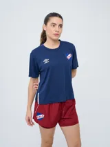 Remera de fútbol Umbro del Club Nacional de Football, modelo Bink para mujer. Diseño azul oscuro con cuello redondo y mangas cortas, con logo de Umbro en el pecho derecho y escudo del club en el pecho izquierdo.