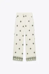 Pantalón de tiro medio color crudo con bordados florales en verde oscuro, cintura elástica ajustable, bolsillos delanteros y pernera ancha.