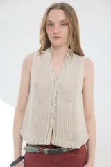 Chaleco sin mangas confeccionado en tejido calado de algodón y acrílico, en color beige. Presenta escote en V con solapas y ribetes de lino a rayitas verticales, cierre frontal con botones forrados y diseño de inspiración sastrera.