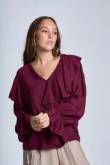 Blusa de color marrón con escote en V, mangas largas abullonadas con puños elásticos y detalles de volados en los hombros y el frente.