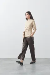 Polera de tejido de punto color beige, con cuello alto, manga larga y detalle de lazo ajustable en la cintura que aporta estructura a la silueta.