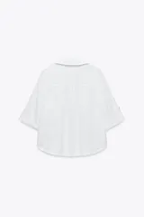 Camisa de lino color celeste claro, con cuello solapa, escote pico, manga corta con vuelta y dos bolsillos de plastrón en el delantero. Cierre frontal con botones.