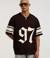 Remera deportiva de algodón color marrón con cuello en V y mangas cortas. Diseño overboxy con estampado de fútbol americano, lettering y rayas contrastantes en blanco.