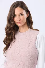 Chaleco tejido de punto grueso en color beige, con cuello redondo y diseño estructurado con detalles de trenzas verticales. Presenta un pequeño aplique de cuero sintético en la parte inferior.