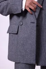 Blazer de corte sastrero en color gris con textura jaspeada. Presenta un diseño de doble botonadura, solapas clásicas y detalle de strass aplicado en una de las solapas. Cuenta con bolsillos laterales con solapa y mangas largas.