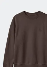 Buzo de cuello redondo con mangas largas y puños elásticos. Presenta un pequeño bordado en el pecho y un diseño liso en color rosado.