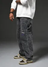 Pantalón jean baggy color gris con efecto stone washed, corte holgado y diseño cargo con múltiples bolsillos y parches bordados en la pierna.