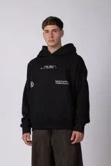 Buzo canguro negro con capucha, confeccionado en algodón frizado de alto gramaje. Presenta estampado gráfico en el pecho con tipografía cursiva y texto, además de un logo circular en la manga. Cuenta con bolsillo frontal tipo canguro, puños y ruedo acanalados.