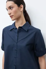 Camisa de algodón color beige claro, con cuello camisero, botones frontales y mangas cortas abullonadas con elástico en el puño.