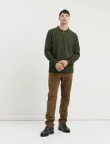 Remera de punto canalé francés color verde militar, con cuello polo, manga larga y cierre frontal de metal.