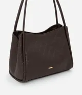 Cartera modelo hobo de gran tamaño, confeccionada en poliuretano con textura geométrica triangular. Presenta asas tubulares largas para llevar al hombro, cierre superior con cremallera y un pequeño aplique metálico dorado en la parte frontal.