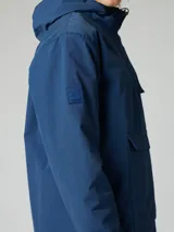 Canguro tipo pullover de color azul, con capucha ajustable, bolsillo frontal tipo canguro y cierre parcial en el cuello. Presenta un diseño funcional con puños elásticos y un bolsillo adicional en la manga.