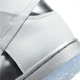 Championes Nike Dunk High con diseño de caña alta, cuerpo en cuero blanco con paneles laterales en negro brillante y detalles metálicos cromados. Presenta suela translúcida y cordones negros.