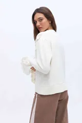 Saco color crudo confeccionado en tejido de punto, con cuello redondo y cierre frontal de botones. Presenta un canesú superior y puños acampanados con detalles de tejido calado y terminaciones de crochet.