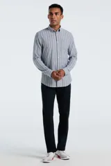 Camisa de manga larga confeccionada en tejido Oxford, con diseño de rayas verticales en tonos gris y azul claro. Presenta cuello abotonado, cierre frontal con botones y un bolsillo en el pecho.
