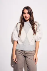 Chaleco de tejido de punto con diseño de rombos en tonos gris claro y blanco. Presenta mangas abullonadas de tela blanca con detalles de encaje y cuello redondo.