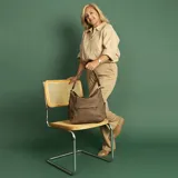 Cartera tipo hobo de cuero sintético color rojo ladrillo, con correa de hombro ajustable. Tiene cierre superior con solapa y broche magnético, bolsillo frontal con cierre, bolsillos laterales con cierre y múltiples bolsillos internos.