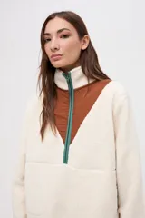 Buzo de sherpa color marrón con diseño de medio cierre frontal. Presenta un panel superior en forma de V en color beige y detalles de vivos en color fucsia en el cierre, cuello y bolsillos laterales. Cuenta con cuello alto y bolsillos frontales.