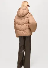 Chaqueta puffer corta color tostado con capucha, bolsillos laterales con ribete, cierre frontal con cremallera y diseño oversize acolchado.