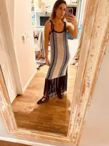 Vestido largo tejido en lurex color beige con diseño vertical y terminación en flecos negros. Breteles finos de cuero intervenido a mano con tientos de cuero plateado.