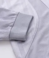 Remera de manga larga estilo deportivo con corte boxy, confeccionada en poliéster. Presenta cuello redondo, paneles laterales en tejido texturizado y estampados gráficos estilo tribal y lettering gótico en el frente.