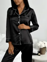 Pijama de satén negro compuesto por una camisa de manga larga con solapas, botones frontales y bolsillo en el pecho, y un pantalón largo a juego. Ambos detalles cuentan con ribetes blancos en contraste.